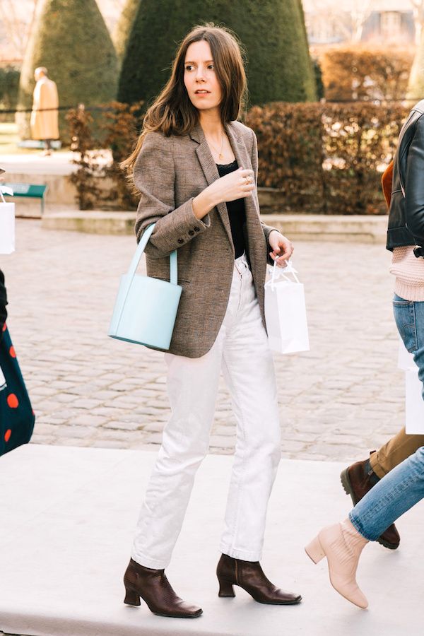 A stylish street style outfit idea with a blazer, baby blue bucket bag, white jeans, and burgundy boots.